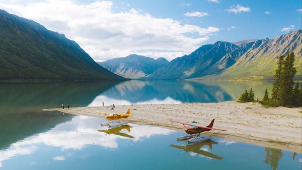 Two float planes are docked along the shore of a pristine blue lake