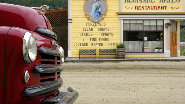 A retro red truck is parked outside a yellow vintage building