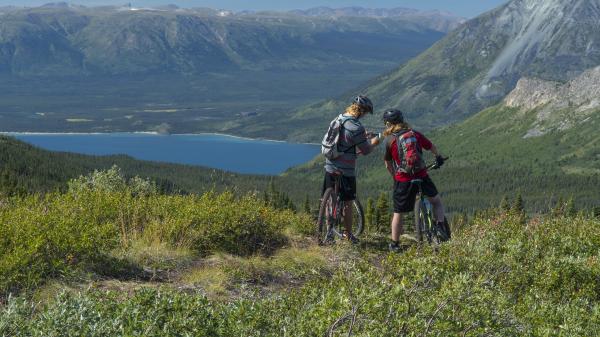Two people at the top of a mountain biking trail overlooking a bright blue lake