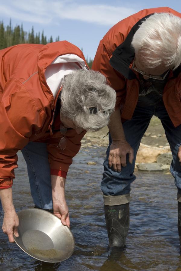 A couple hunches over a gold pan in a river
