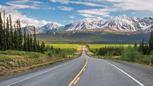 Alaska highway with snow-capped mountains on the horizon