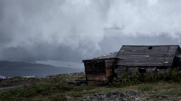 An old cabin sits among clouds at the top of a mountain