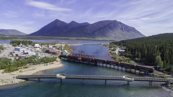 A bridge and railroad crossing extend over a lake with a small town to the left and mountains to the back