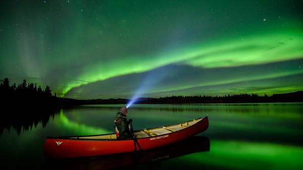 A canoer watches the northern lights from a lake