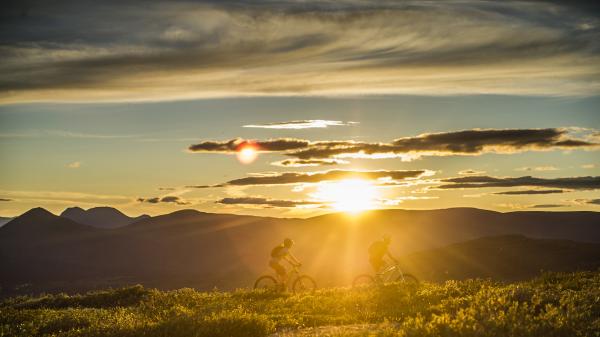 Two bikers ride across the sunny horizon of a mountaintop