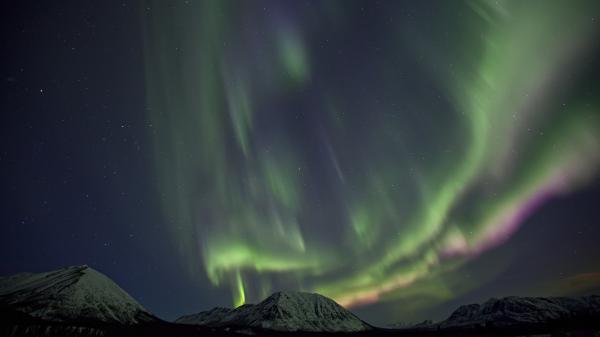 Green northern lights shine over snow capped mountains