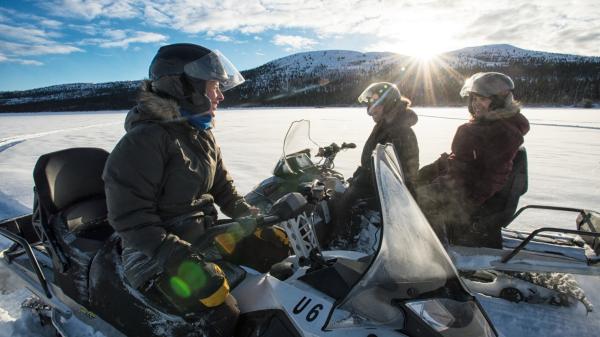 Three people on snowmobiles laugh and smile