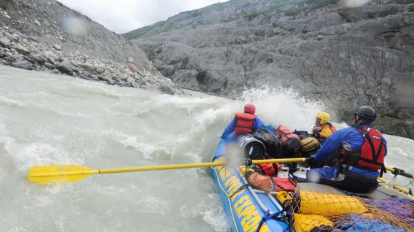 Three people face rapids in a blue raft 