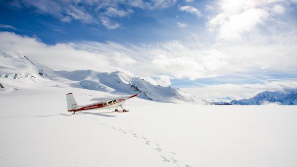 A small plane lands on a mountain under a blue sky