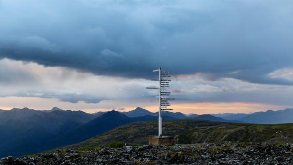 A sign post pointing to cities in many directions stands on a mountaintop