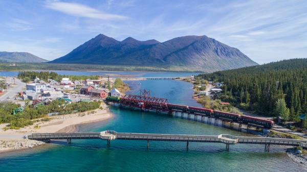 A drone shot of a large river connecting two lakes with two red bridges stretching across and tall mountains in the background