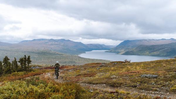 A mountain biker on top of a mountain with a large river and mountain valley behind them