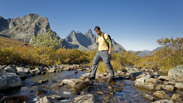 A man in a yellow shirt and grey pants crosses a creek