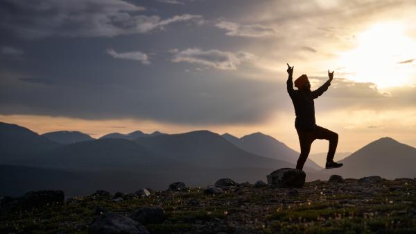 A man dancing on top of a mountain at sunset