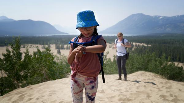 A child looks at their watch at the top of a sand dune in the Carcross Desert.