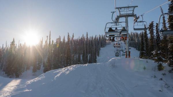 A chairlift goes up a snow covered mountain in the sunshine under a blue sky