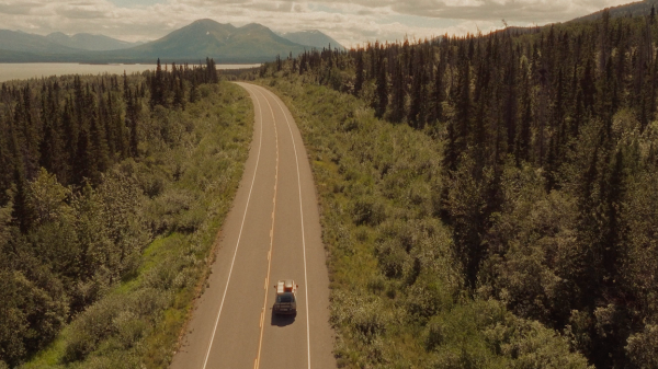 A car driving on a highway in the Yukon during summer