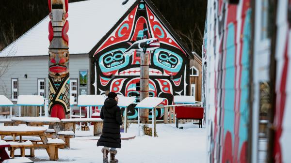 A woman walks in front of totem pole at the Carcross Commons in winter time.