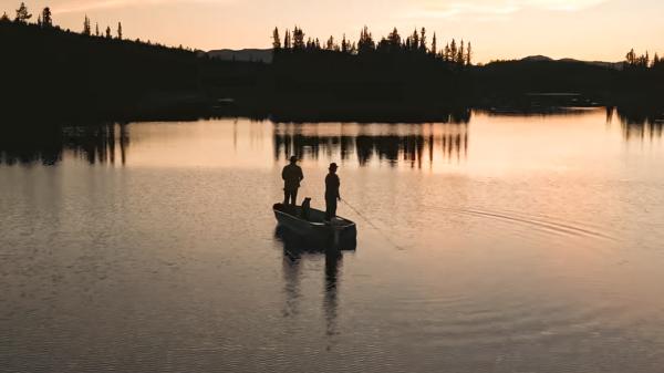 2 people fly fishing on a Yukon lake off a small boat during a sunset.