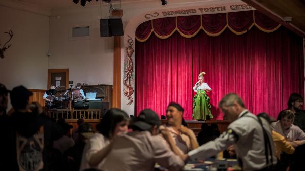 Diamond Tooth Gertie sings on stage in front of red curtains for the gambling hall audience