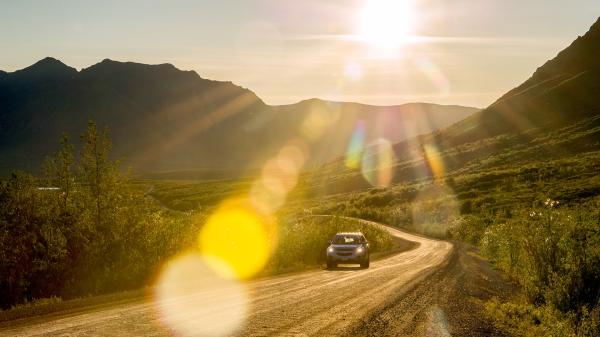 A driver cruises down the highway under the midnight sun