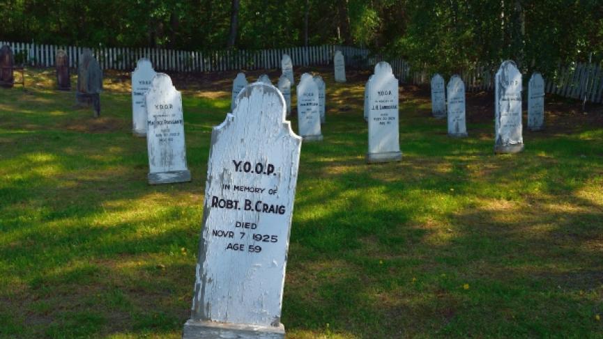 Gravestones stand in the grass of the Dawson City Cemetaries