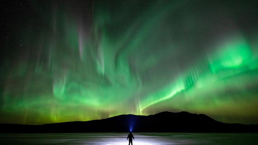 Skier on frozen lake with Northern lights