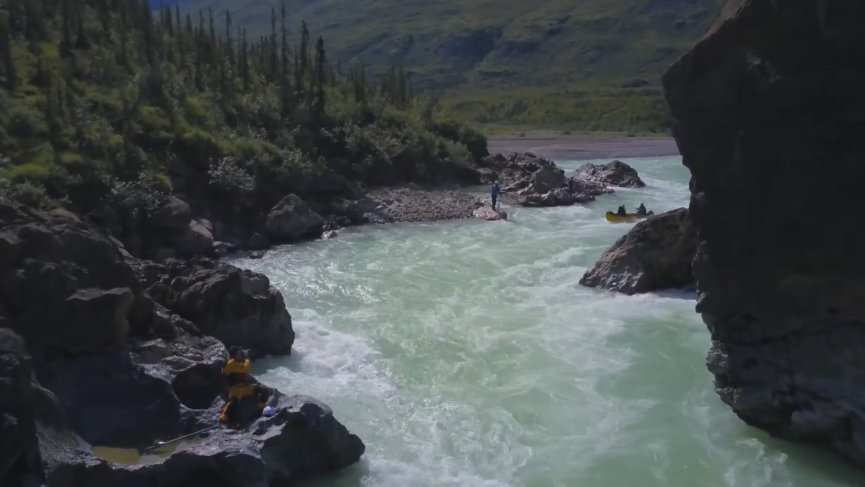 Cliff walls frame the scene as a canoe is paddle down class II+ whitewater in the snake canyon