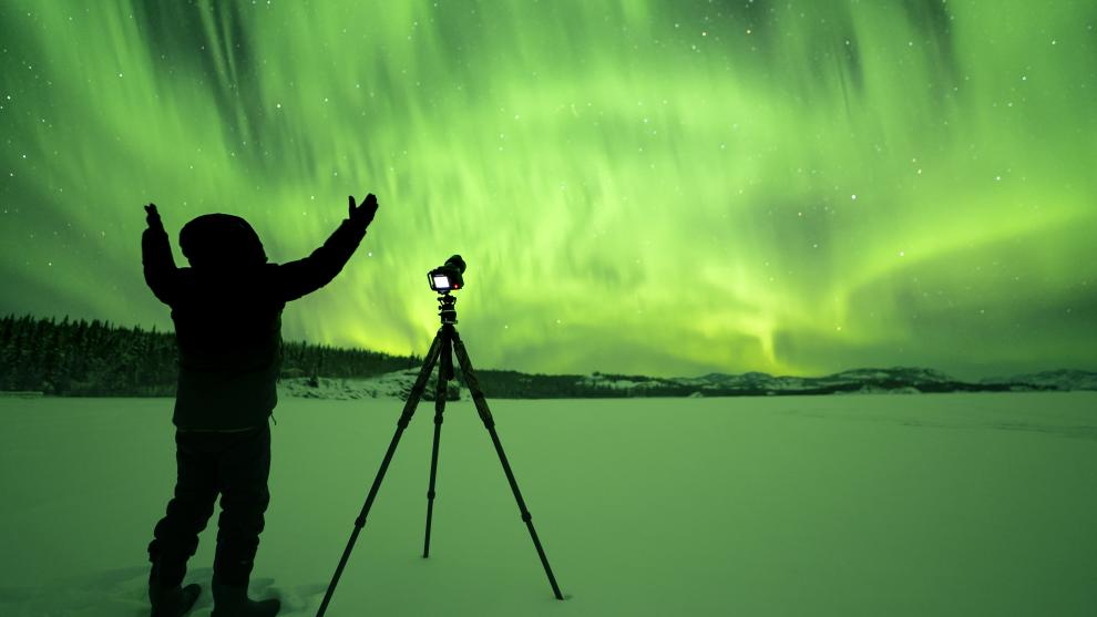A person photographs spectacular green aurora borealis in the Yukon