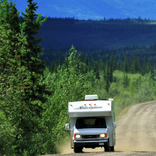 A truck and camper drives down a dirt road lined with trees 