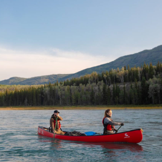 Two people in a red canoe paddle along a river 