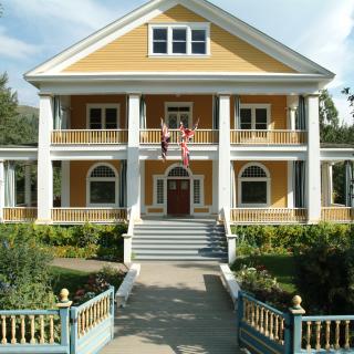 A yellow house with a white picket fence, green front lawn and tall white pillars