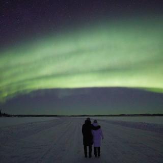Couple stands together under a green arc of northern lights