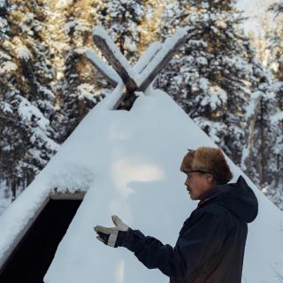 man standing outside a first nation hut
