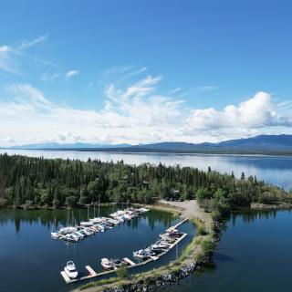 Drone shot of marina, clear blue water, treed campground, surrounded by scenic mountains 
