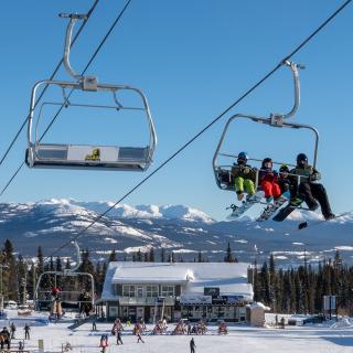 View of the lodge with mountains in the background, and a group of people riding the chairlift.