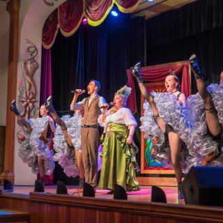 Diamond Tooth Gertie sings and cancan dancers high-kick on the gambling hall stage