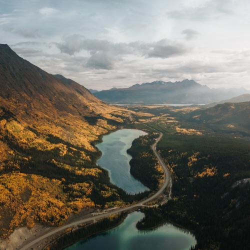 Two teal lakes on either side of a highway next to a mountainside