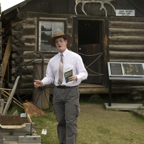 A man performs a historical recitation in front of a log cabin