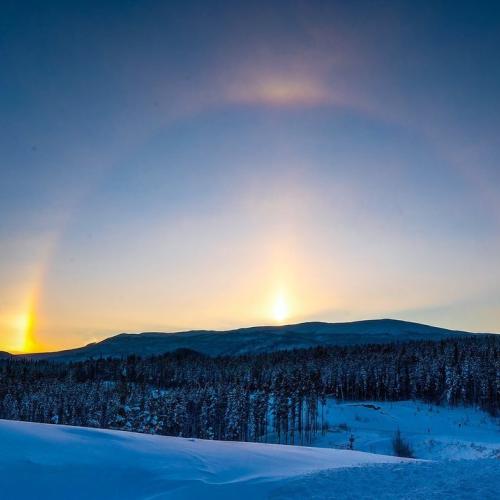 A sundog shines over a mountain along the horizon. The winter sky is dark blue. 