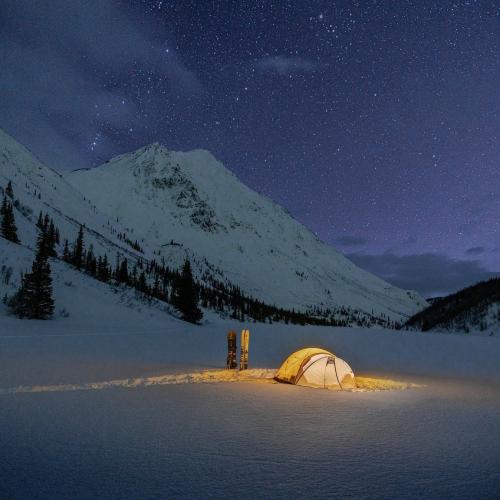 A tent glows under the starry purple sky