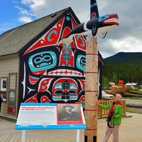 A woman stands in front of a totem pole in carcross