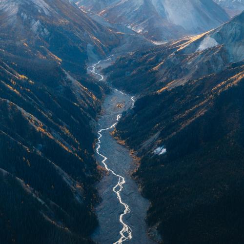 A glacial river runs through a mountain valley toward snow covered mountain range