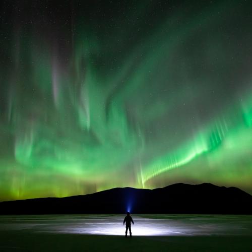 Skier on frozen lake with Northern lights