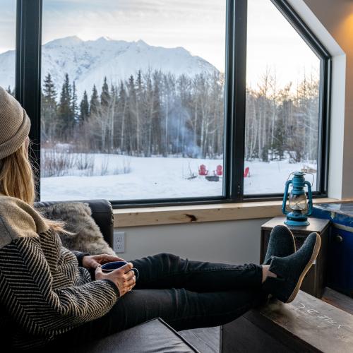 A woman enjoying a cup of coffee while looking outside the window in winter.
