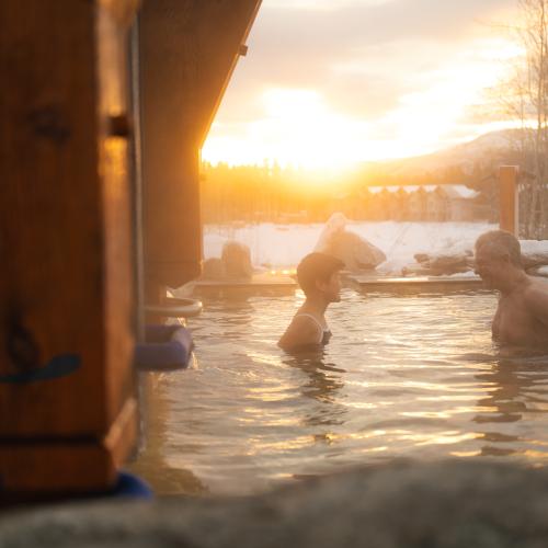 Relaxing in outdoor hot springs at Eclipse Nordic Spa during a winter sunset in Yukon.