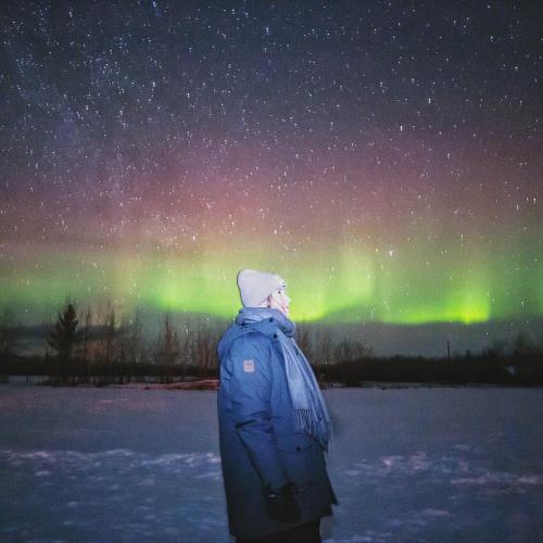 A person standing under the northern lights dressed warmly