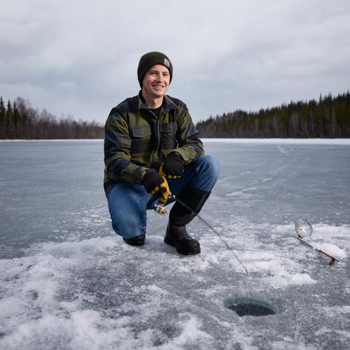 Gavin Wintersinnot sitting on a frozen lake while smiling at the camera. 