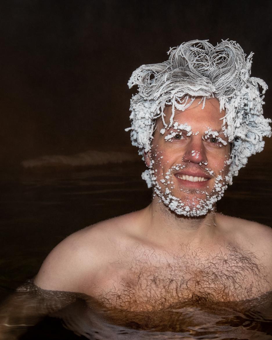 A man with frozen hair stands in a hot spring in the dark of night