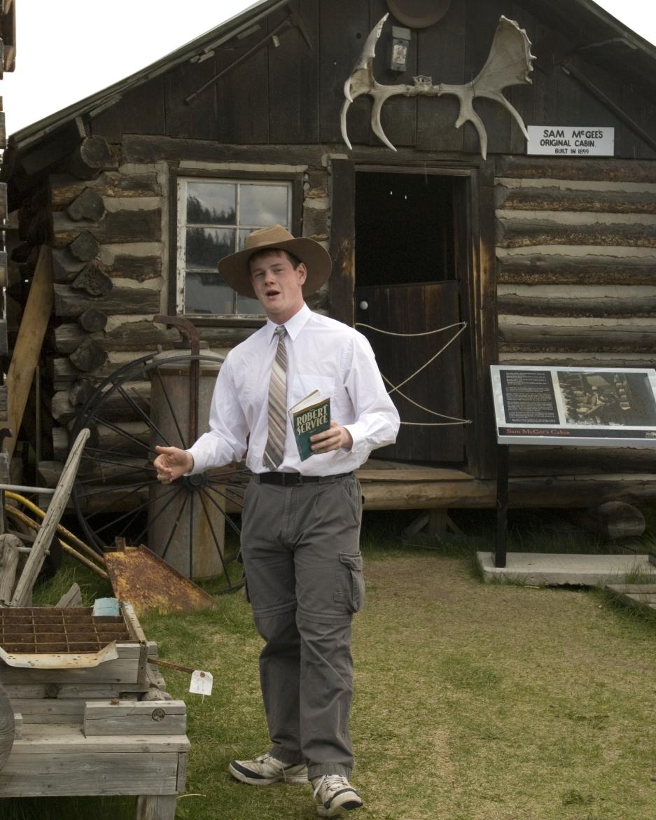 A man performs a historical recitation in front of a log cabin